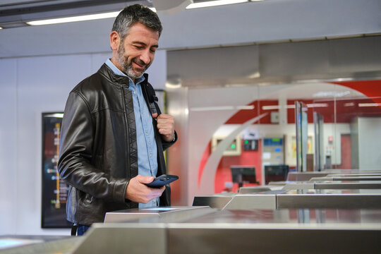 middle aged Man using smartphone for contactless payment at subway turnstile