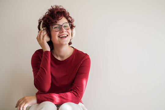 Curly red hair girl with eyeglasses and headphones laughing indoors
