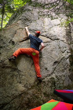 A male climber working his way up a route on a boulder in NH