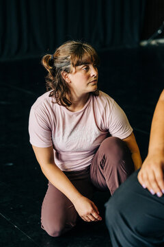 Woman kneeling, listening intently during dance rehearsal
