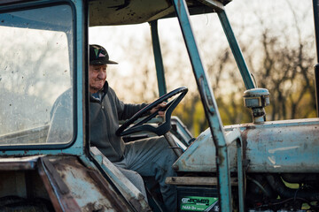 Elderly farmer driving a tractor at sunset on a farm in autumn