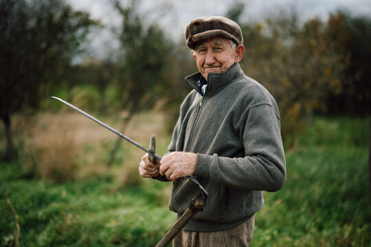 Elderly farmer holds a tool in a lush green field