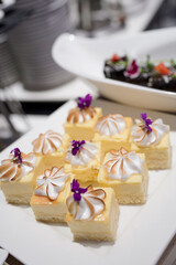 Mini lemon cheese cakes tartlets topped with toasted meringue and purple Viola edible flower on a white square serving platter