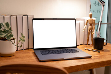 Modern laptop with a blank white screen mockup placed on a wooden desk in a stylish, cluttered workspace with books and decor.