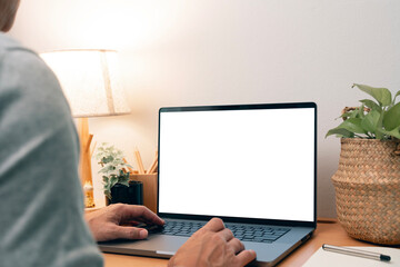 A man working on a laptop with a blank white screen, surrounded by a warm, minimalist home office setting.
