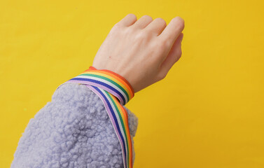 Woman's hand wrapped in a rainbow ribbon on a yellow background. Solidarity, LGBT community.