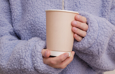 Craft eco disposable cardboad cup in a female hands wearing a cozy sherpa sweatshirt. Coffee or tea drink