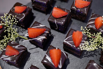 chocolate cake with strawberry, Indulgent chocolate petite fours on a dark slate, decorated with strawberry and white drizzle, featuring white baby's breath