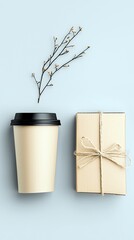 A simple arrangement featuring a paper coffee cup with a black lid, a small gift box tied with twine, and a bare branch with tiny buds, all set against a soft b