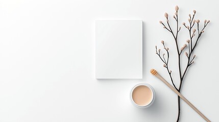 A minimalist composition featuring a blank white canvas, a jar of light-colored cosmetic cream, and a decorative branch with small buds, arranged on a clean whi