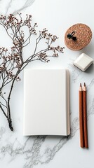 A minimalist flat lay composition featuring a blank notebook, dried branches, pencils, an eraser, and a cork lid on a marble surface.