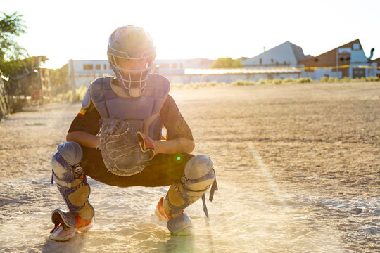 Youth baseball catcher playing on dusty field at sunset