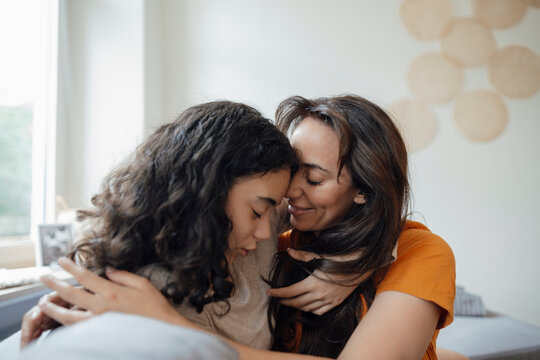 Mother with eyes closed embracing daughter on sofa at home