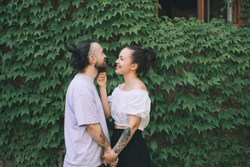 Happy hipster couple holding hands standing by green ivy plants