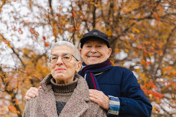 Smiling elderly couple under tree at autumn park