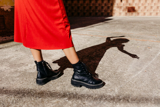 Young woman wearing red dress and black boots, playing with her shadow on the floor