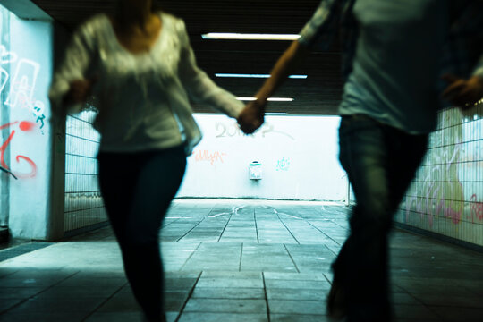 Young couple running hand in hand in a dark underpass, partial view