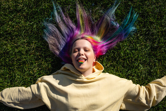 Portrait of young woman with dyed hair and rainbow candy lying on meadow