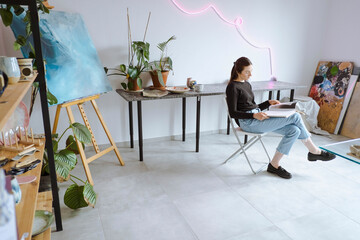 Artist reading book sitting on chair at workshop
