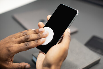 Hand of unrecognizable black businessman with alcohol gel or sanitizer for cleaning hand and protecting against coronavirus or covid-19, manager using modern smartphone at office, closeup photo