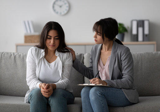 A professional psychologist provides emotional support to an unhappy middle eastern woman during a therapy session. The setting is calm and encourages open dialogue for mental health improvement.