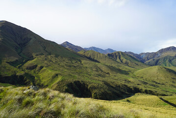 Naklejka premium Danseys Pass Kakanui Range tussock-covered high country mountains in springtime under a blue cloudy sky. Waitaki and Central Otago in the South Island of New Zealand.
