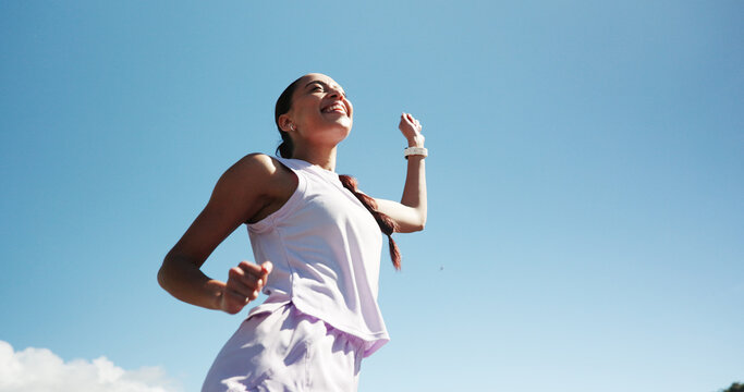 Happy woman, fitness and winning with blue sky for race, sprint challenge or marathon in city. Low angle, female person or runner with smile for victory, achievement or accomplishment on mockup space