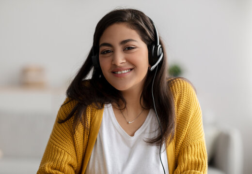 A warm and friendly Arab customer service representative is wearing a headset and smiling while looking directly at the camera. She is working in a call center, providing support.
