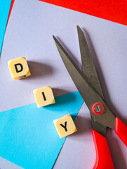 vertical flat lay of scissors and letter dice spelling DIY on vibrant colored paper