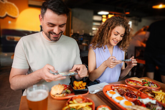 Young Couple Taking Pictures of Food in Restaurant - Powered by Adobe