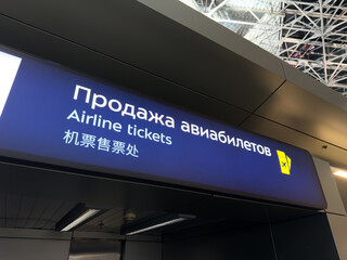 Ticket counter at airport. The Airplane Tickets sign in Russian, English, and Chinese for multicultural navigation in modern airport. Buying ticket in unknown city to travel the world