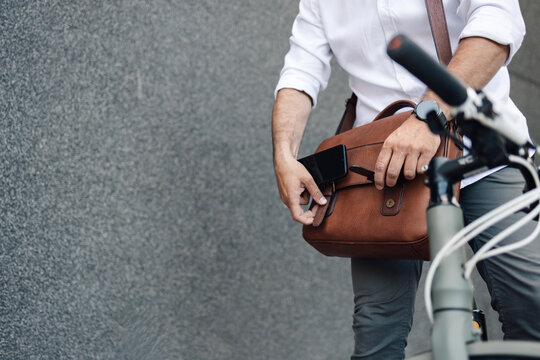 Businessman reaching into briefcase, holding smartphone by bicycle