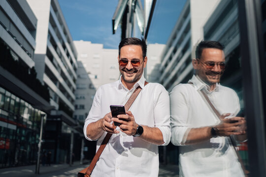 Happy businessman smiling and using phone in city