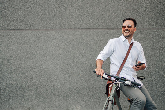 Smiling man commuting by bike holding phone - Powered by Adobe