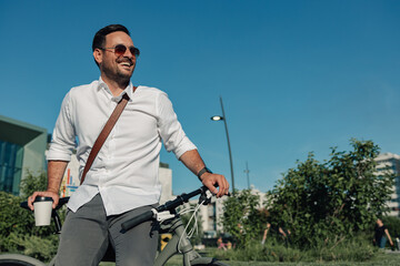 Happy businessman commuting by bicycle enjoying morning coffee