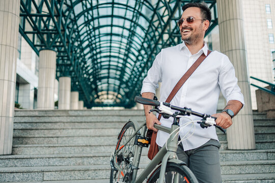 Happy businessman walking bicycle up urban stairs