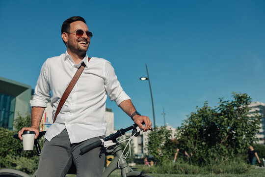 Happy businessman commuting by bicycle enjoying morning coffee
