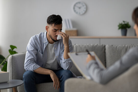 A stressed Arab man shares his problems and cries during a psychotherapy session at a clinic. A psychologist listens attentively as he seeks professional help with his mental health.