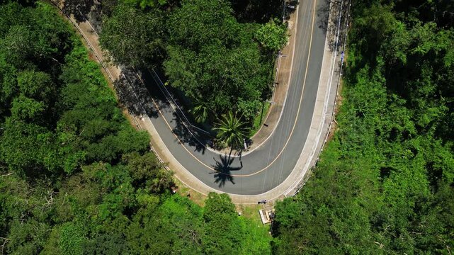 Top‑view aerial showcasing the winding Mount Samat Road cutting through dense tropical forest, framed by lush greenery and scenic mountain terrain in Pilar, Bataan, Philippines.