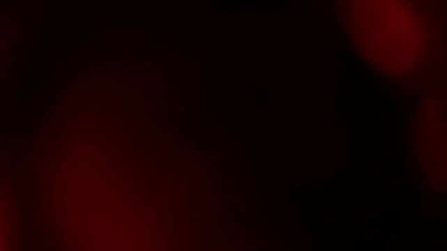 A soft, warm red light leak gently washes over a black background. Perfect for creating a cinematic, vintage, or romantic film burn overlay effect
