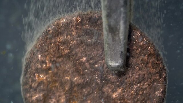 Bubbles rise from ancient Roman coin undergoing electrolytic cleaning.