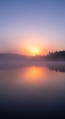 Obraz premium Sunrise over a misty lake with vibrant orange and purple hues reflecting on the water.
