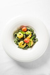 A close-up vertical studio shot of vibrant green spinach tagliatelle pasta with prawns, cherry tomatoes, and basil leaves in a white bowl.