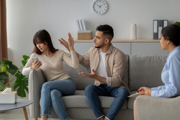 An angry couple discusses their relationship issues with a therapist. The man gestures expressively...