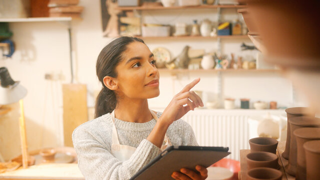 Female Potter In Ceramics Studio Checking Orders Using Digital Tablet