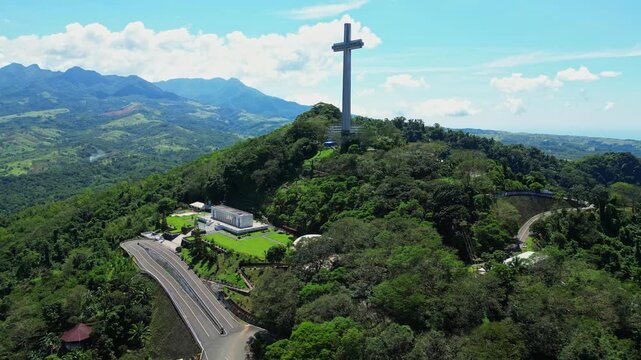 Slow left pan aerial showcasing the towering Mt. Samat National Shrine surrounded by lush forested hills, with sweeping views of valleys and mountains in Pilar, Bataan, Philippines.