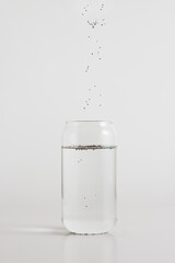 Chia seeds pouring into a glass of water on a white background