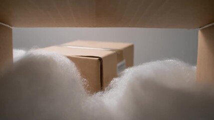 A carefully protected cardboard package, securely nestled in a fluffy white cushion, awaits its journey within a larger shipping container, symbolizing safe transit and reliable delivery services