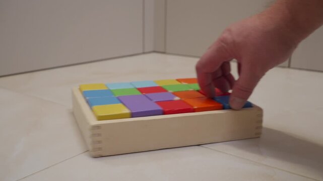 A wooden box containing colored wooden blocks is pushed across a hard tile floor. The bottom of the box drags and slides, creating a low scrape.