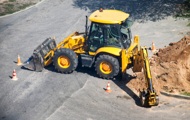 Yellow modern excavator near a hole on an asphalt road. Concept of emergency service in the city to...